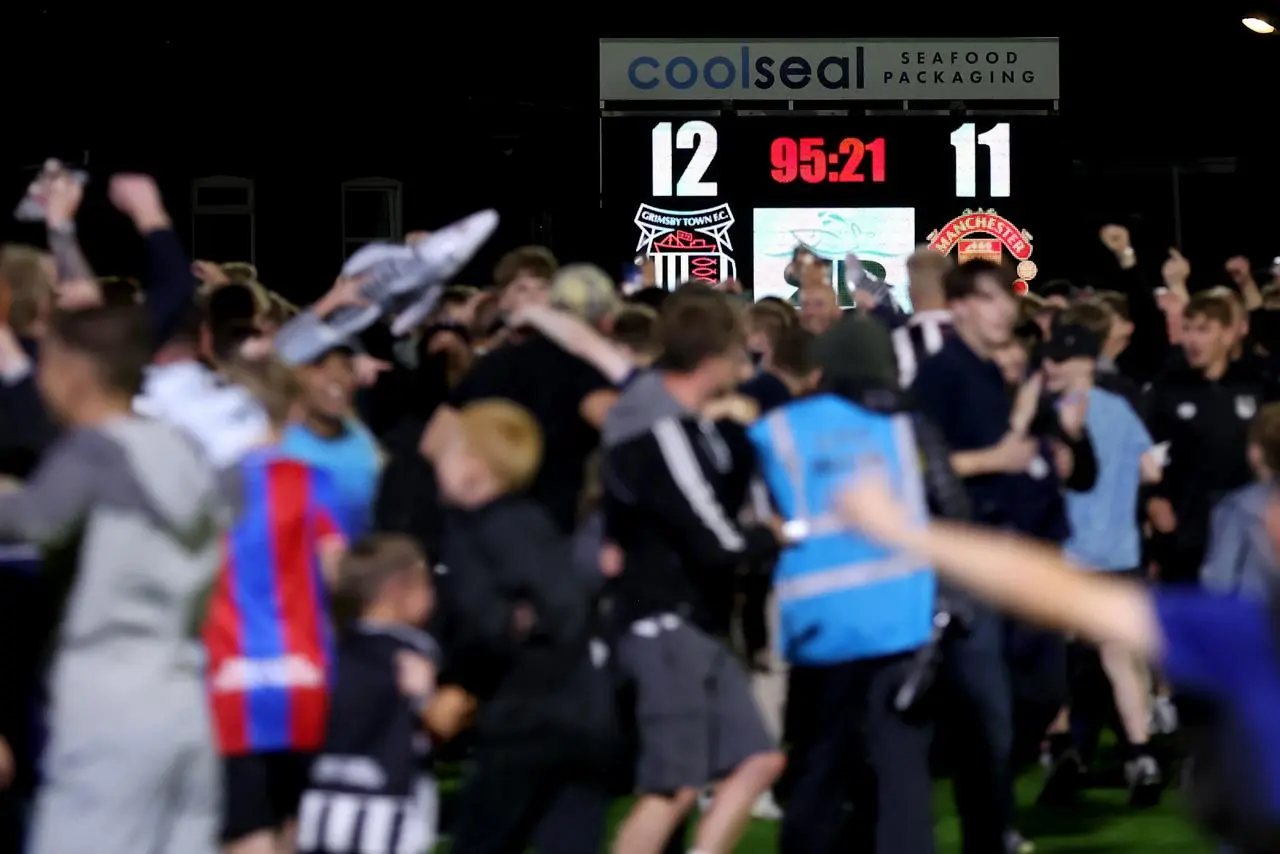 Grimsby fans celebrate their victory in the shootout against Manchester United as the scoreboard shows the final score