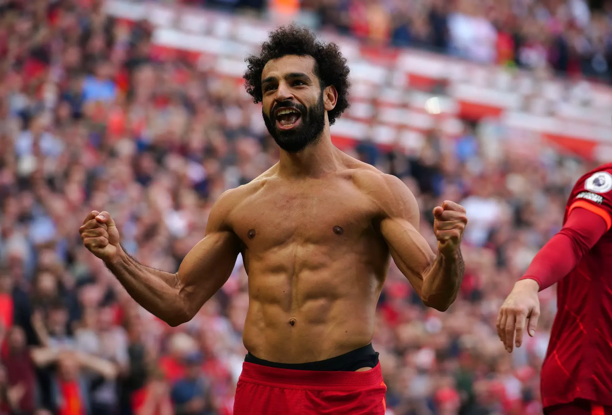 A shirtless Mo Salah celebrates in front of the Liverpool fans