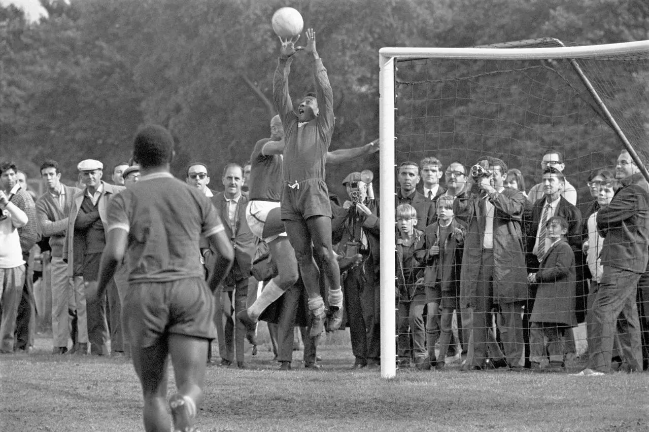 Makeshift goalkeeper Pele leaps to catch a ball during a training session for the 1966 World Cup. The striker had taken a turn between the sticks as a small crowd watched on