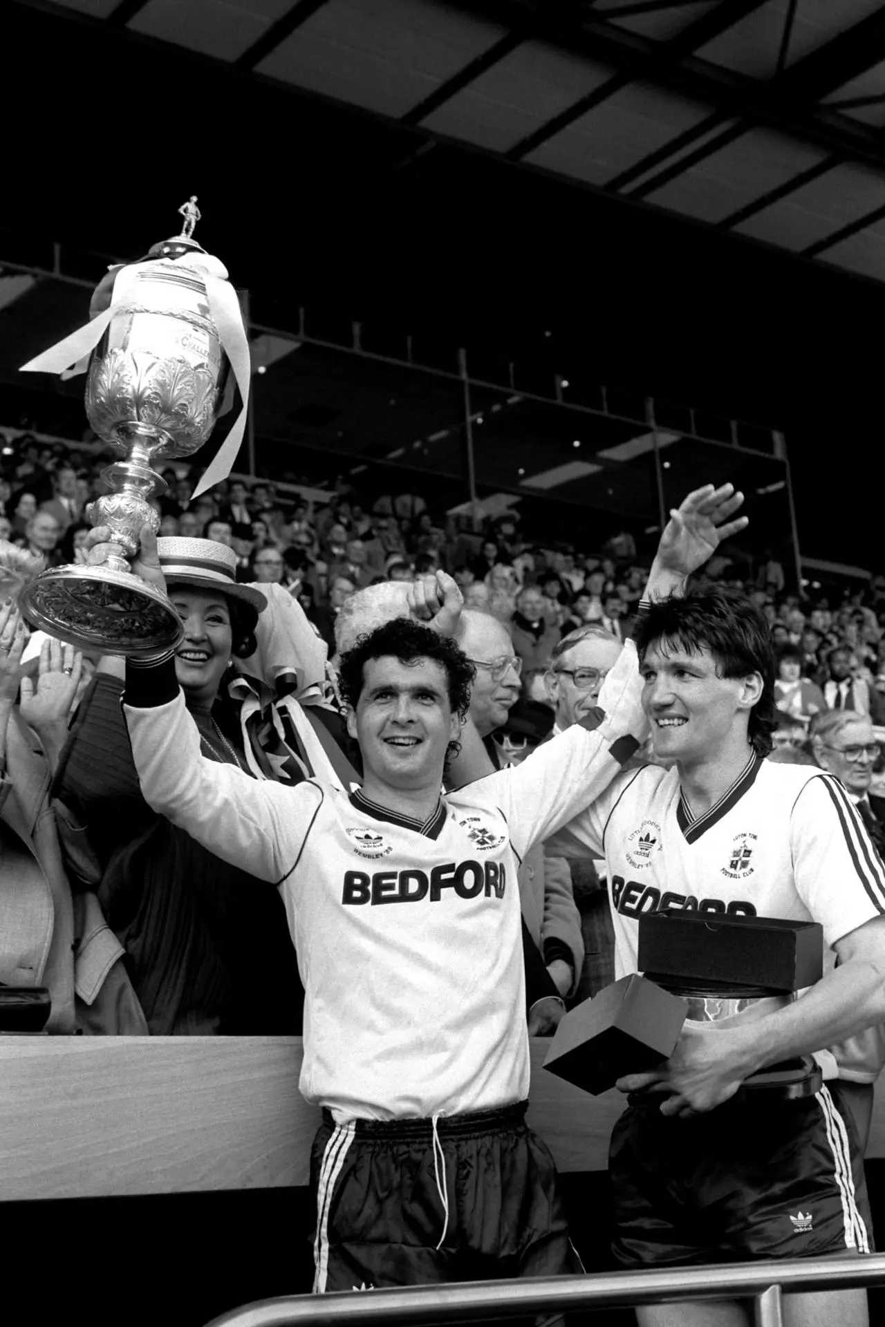 Luton captain Steve Foster (left) lifts the Littlewoods Cup watched by Mick Harford (right)