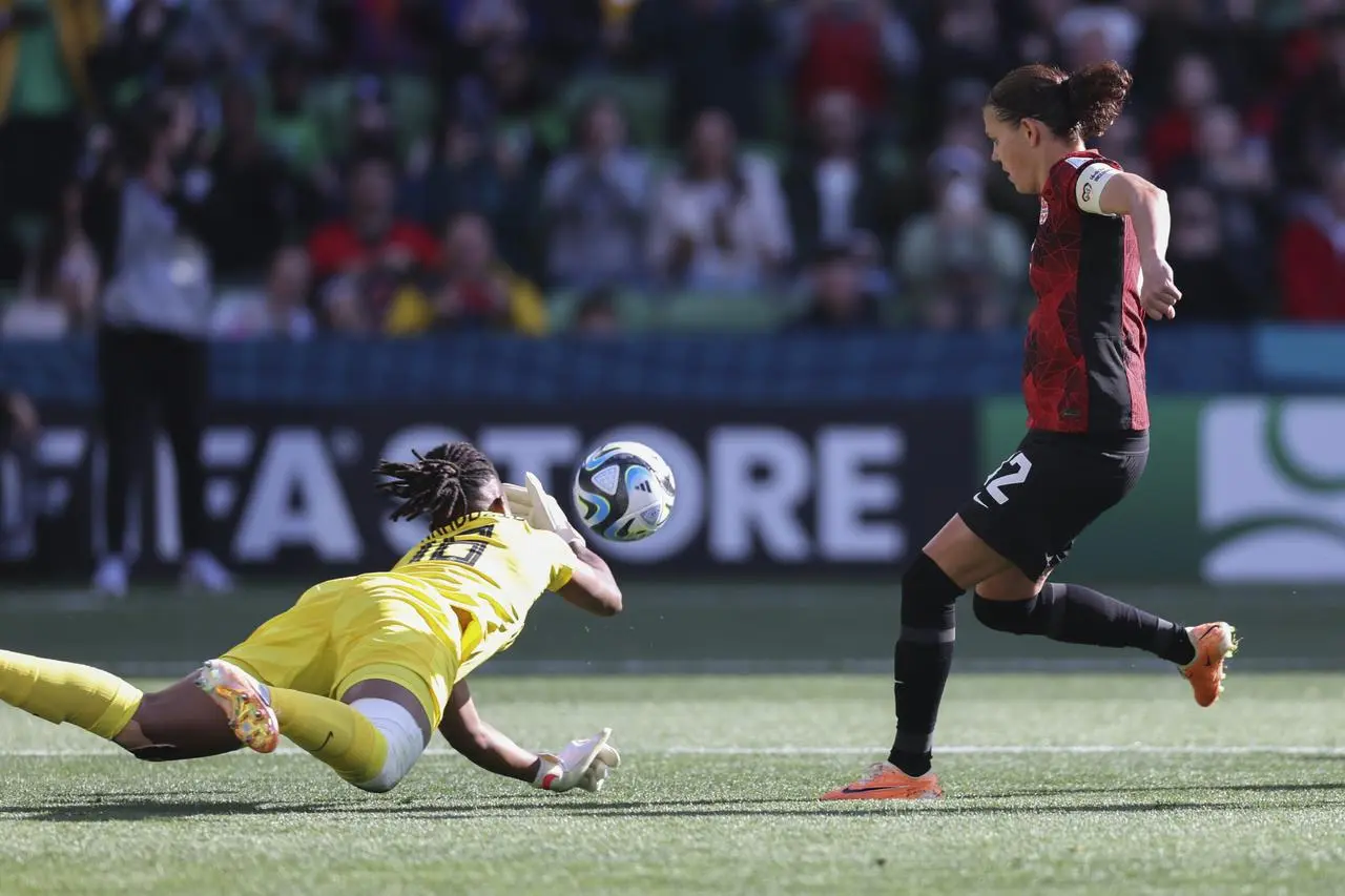 Nigeria goalkeeper Chiamaka Nnadozie, left, tips the ball away from Christine Sinclair, right, after saving the Canada striker's penalty