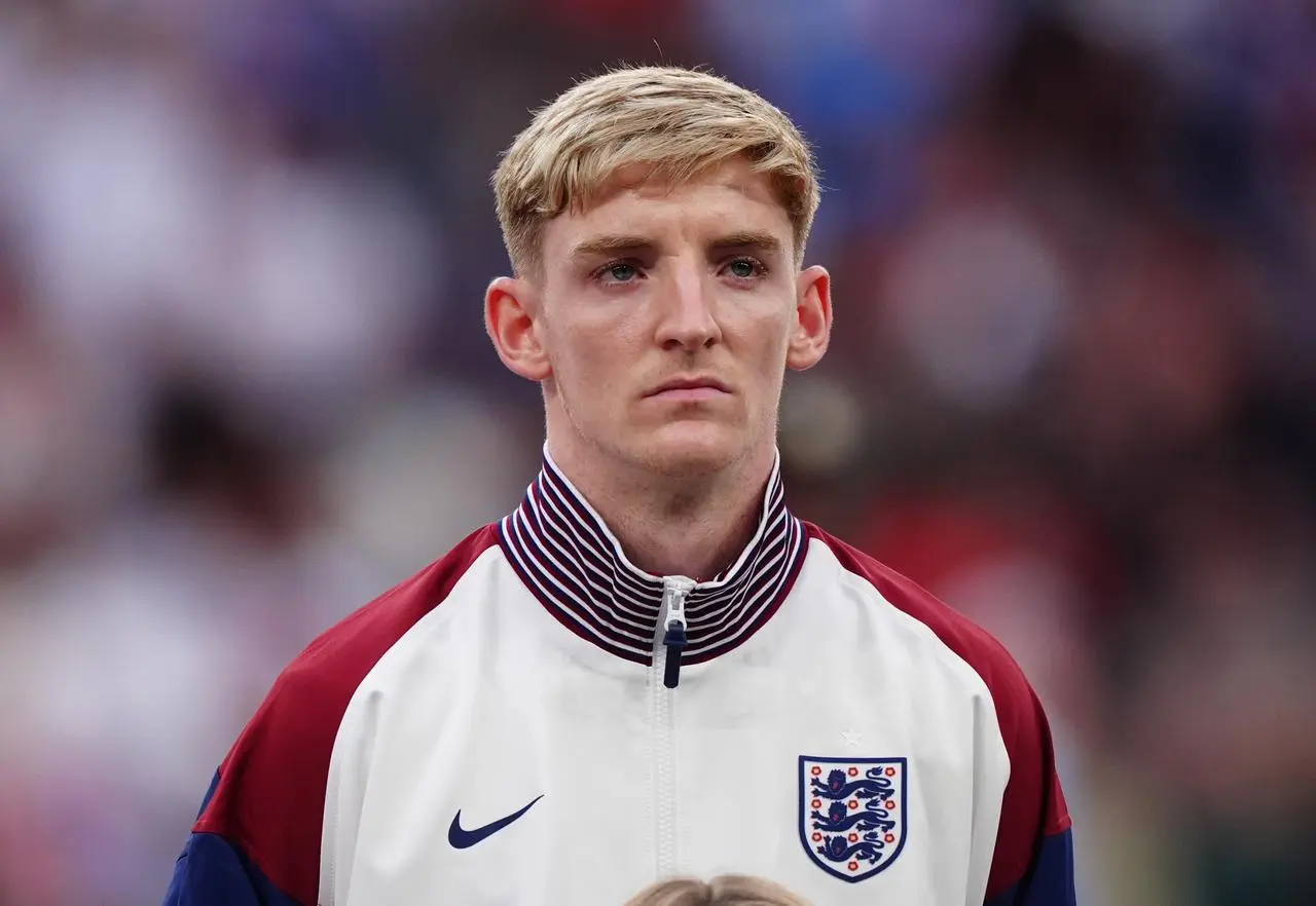 Anthony Gordon stands for the national anthem in an England tracksuit