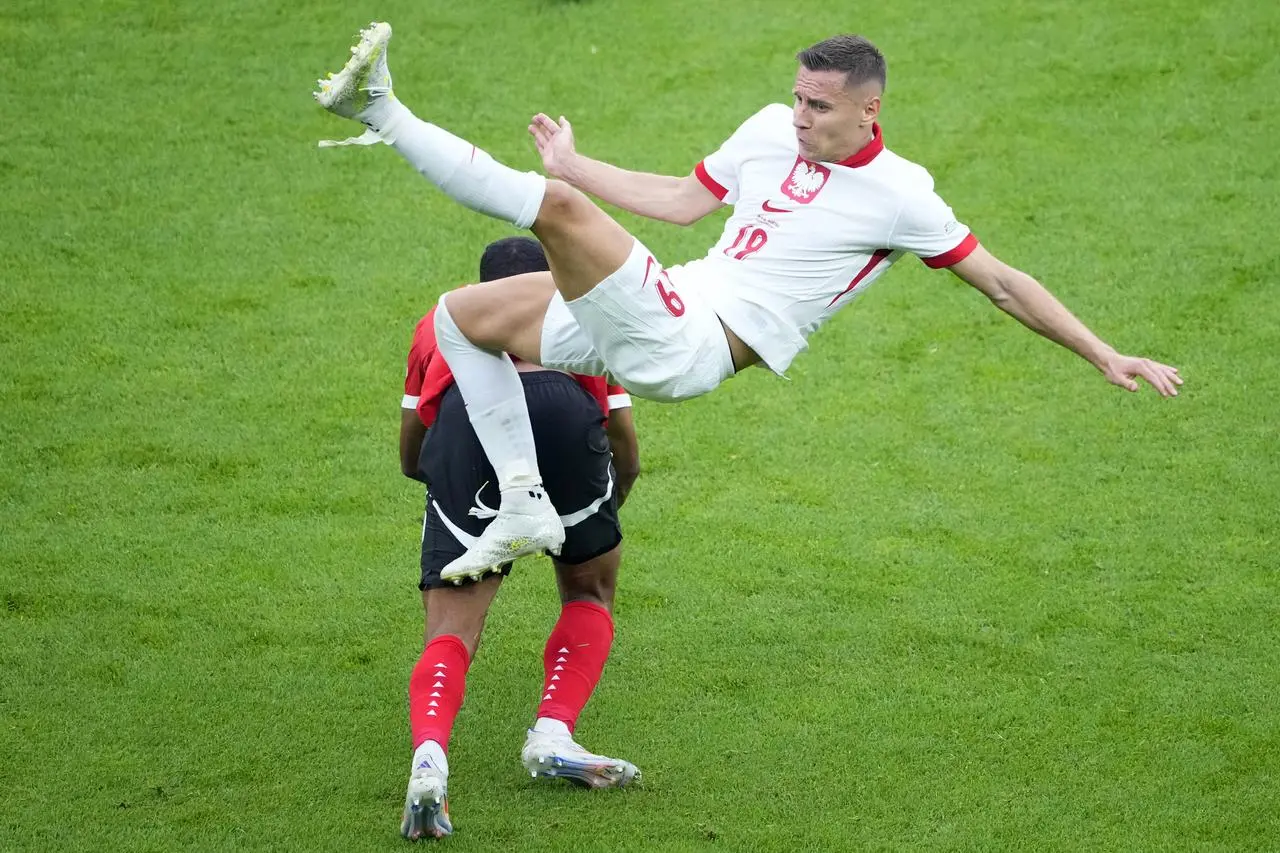 Poland’s Przemyslaw Frankowski is lifted off the ground by a challenge from Austria’s Philipp Mwene