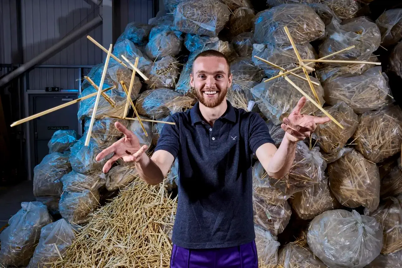 Tom Davies throws handfuls of chopsticks in front of a stack of bags of used chopsticks