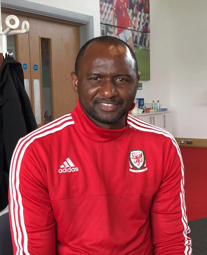 Patrick Vieira smiles at the camera wearing a Wales training top