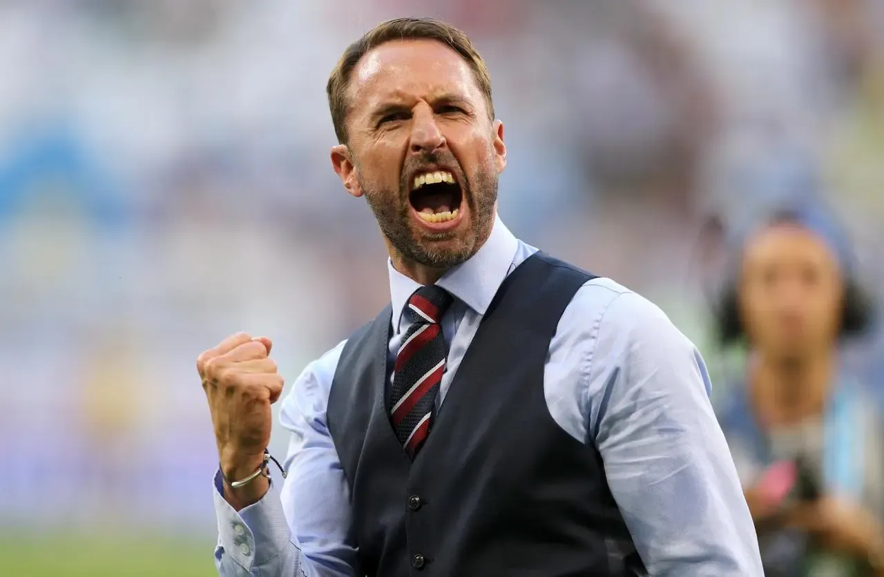 England manager Gareth Southgate, wearing his famous waistcoat, shirt and tie, clenches a fist and roars as he celebrates victory after the World Cup quarter-final win over Sweden in 2018