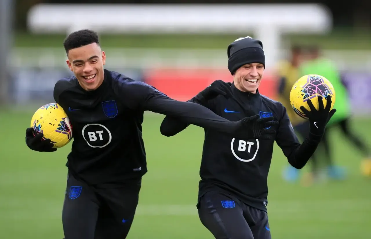 England duo Mason Greenwood and Phil Foden, both holding a ball in one hand, laugh during a training session at St George’s Park