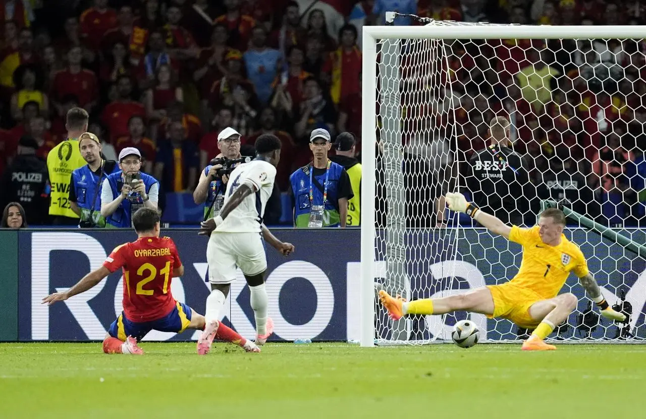 Spain’s Mikel Oyarzabal, left, slides in front of England defender Marc Guehi to score the winning goal in the Euro 2024 final as goalkeeper Jordan Pickford, right, is beaten