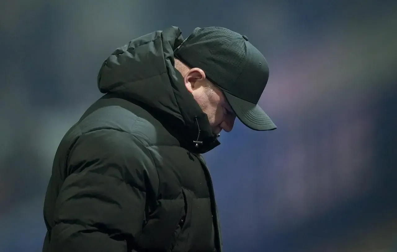 Wayne Rooney, with his face covered by his coat and hat, bows his head during a Birmingham match