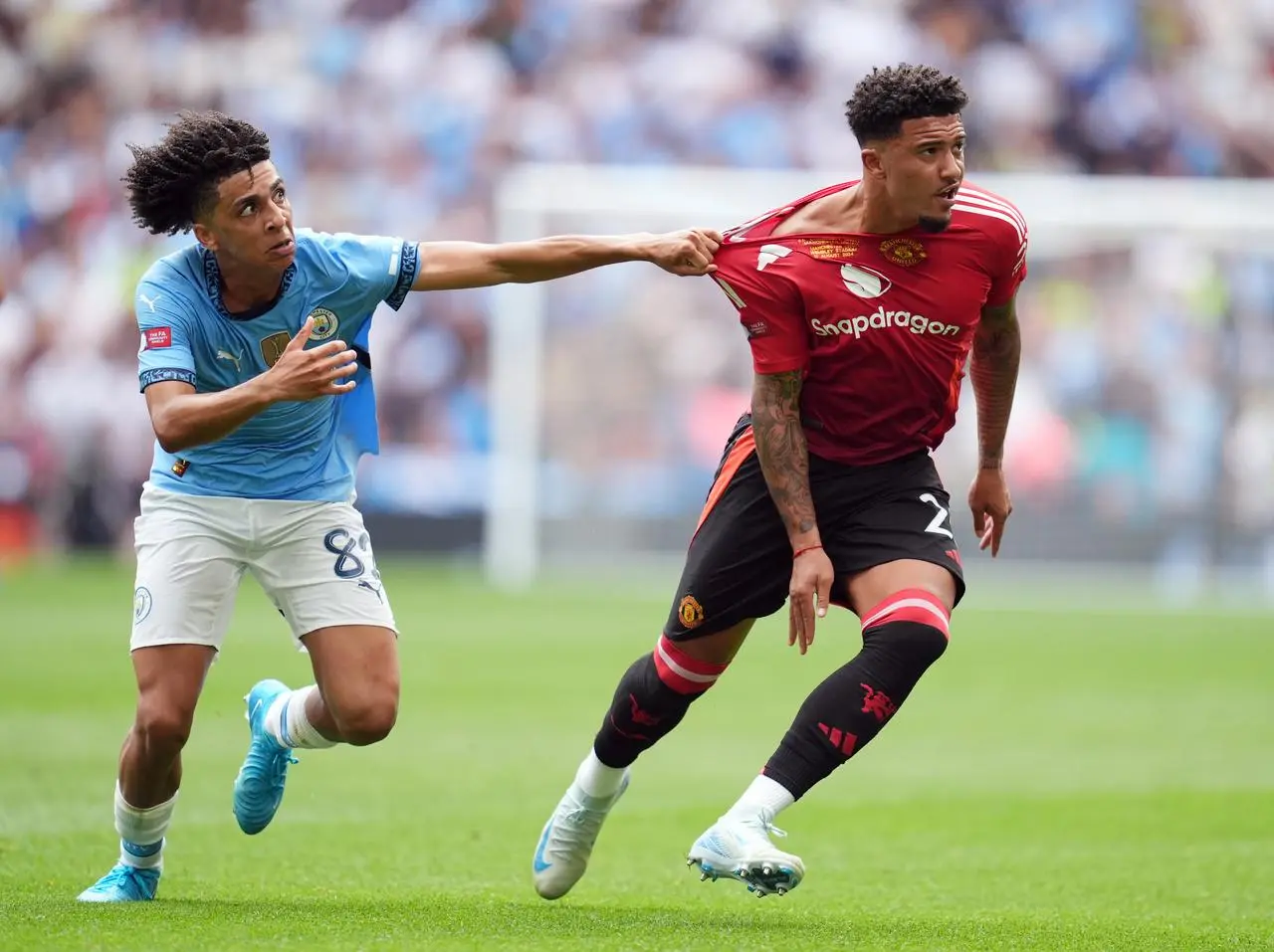 Manchester City’s Rico Lewis pulls on the shirt of Manchester United’s Jadon Sancho