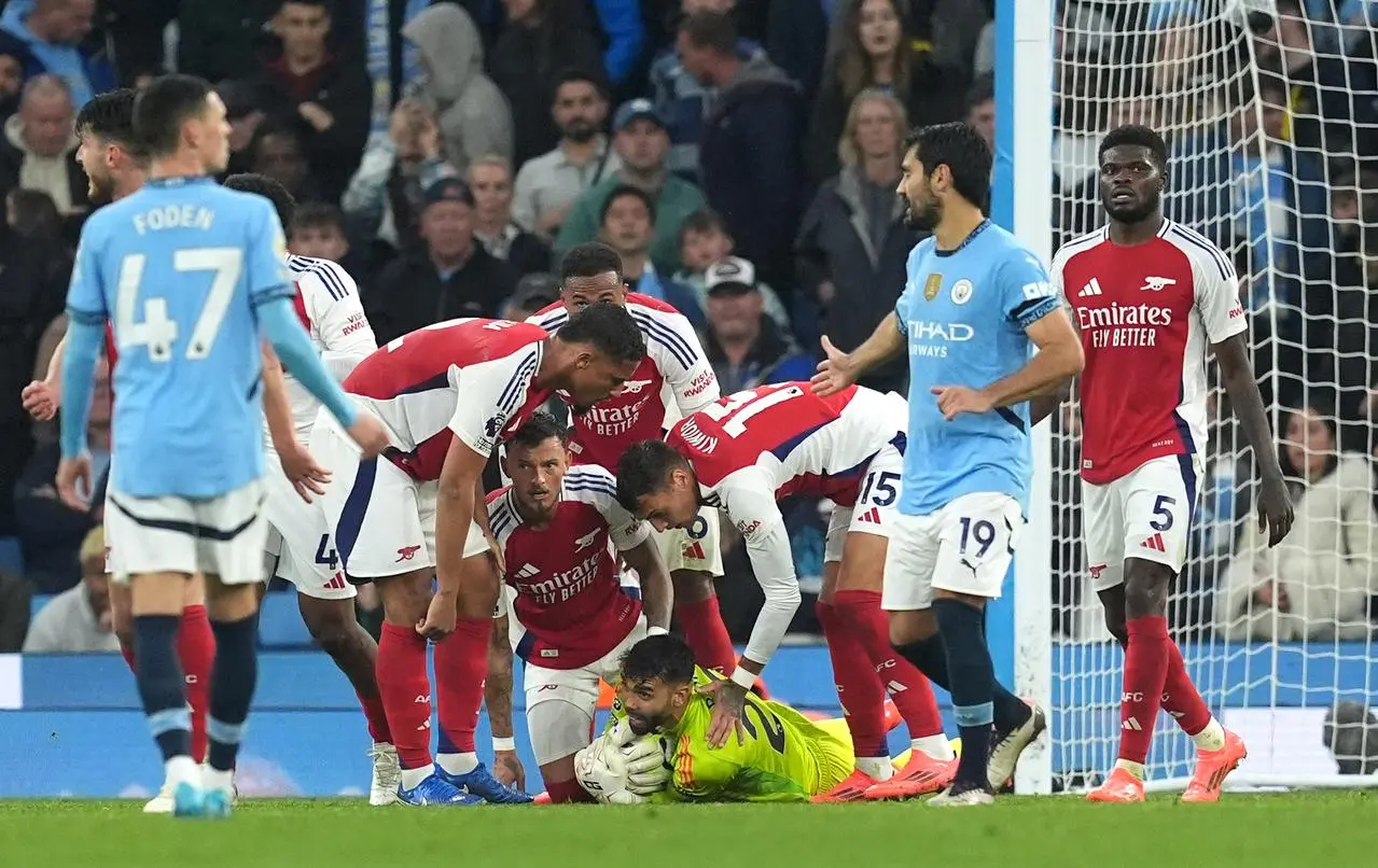 Arsenal players lean in to congratulate goalkeeper David Raya, on ground, after he made a save against Manchester City