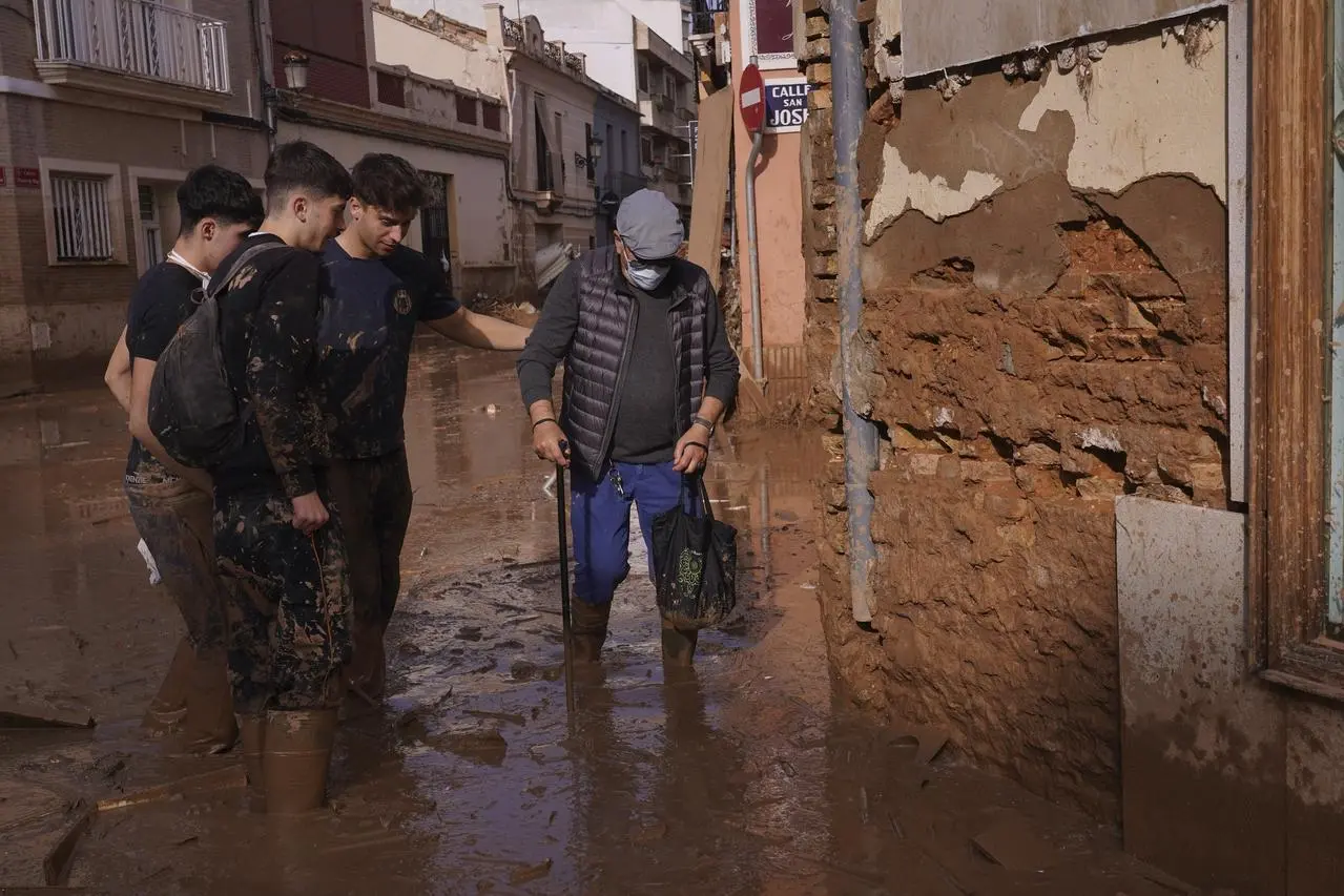 Youths help a man walk in the mud after floods in Paiporta, near Valencia, Spain (Alberto Saiz/AP)