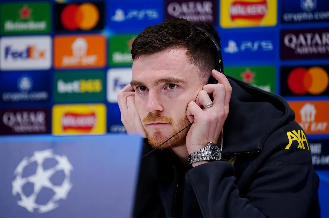 Andy Robertson holds headphones on his ears as he speaks to the media