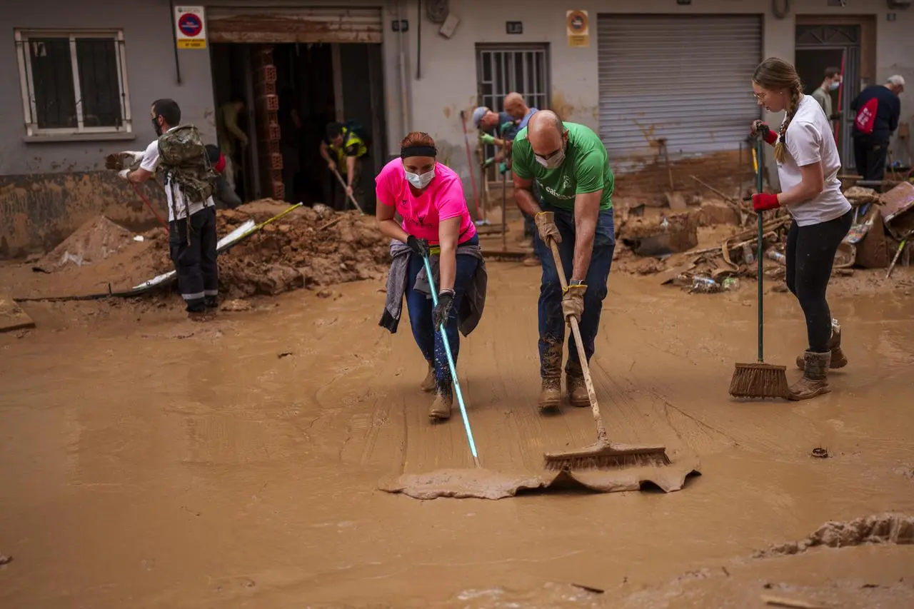 People clean the street of mud in an area affected by floods in Valencia, Spain, Saturday, Nov. 2, 2024.