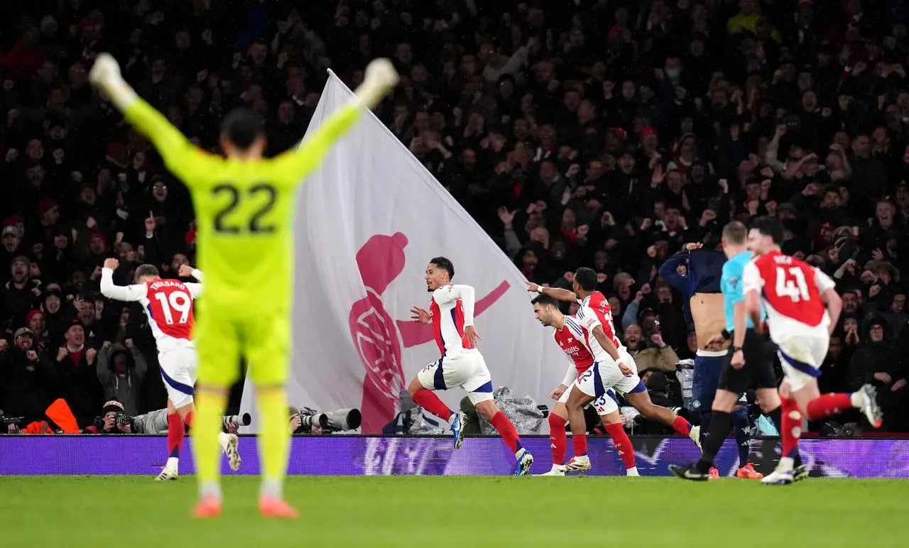 David Raya stands with his hands in the air as he watches William Saliba celebrate scoring