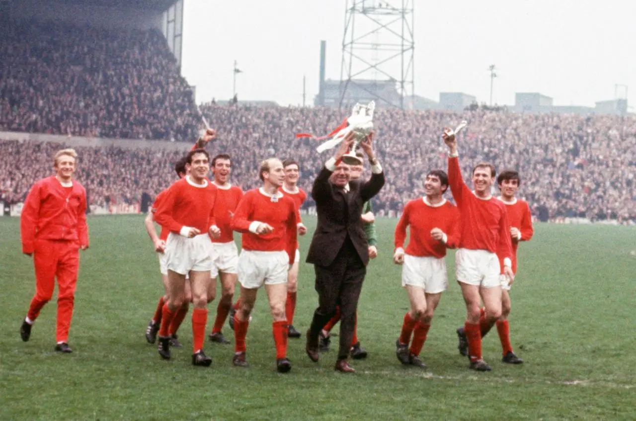 Manchester United manager Matt Busby (fourth right) holds the League Championship trophy aloft as he and his players parade it