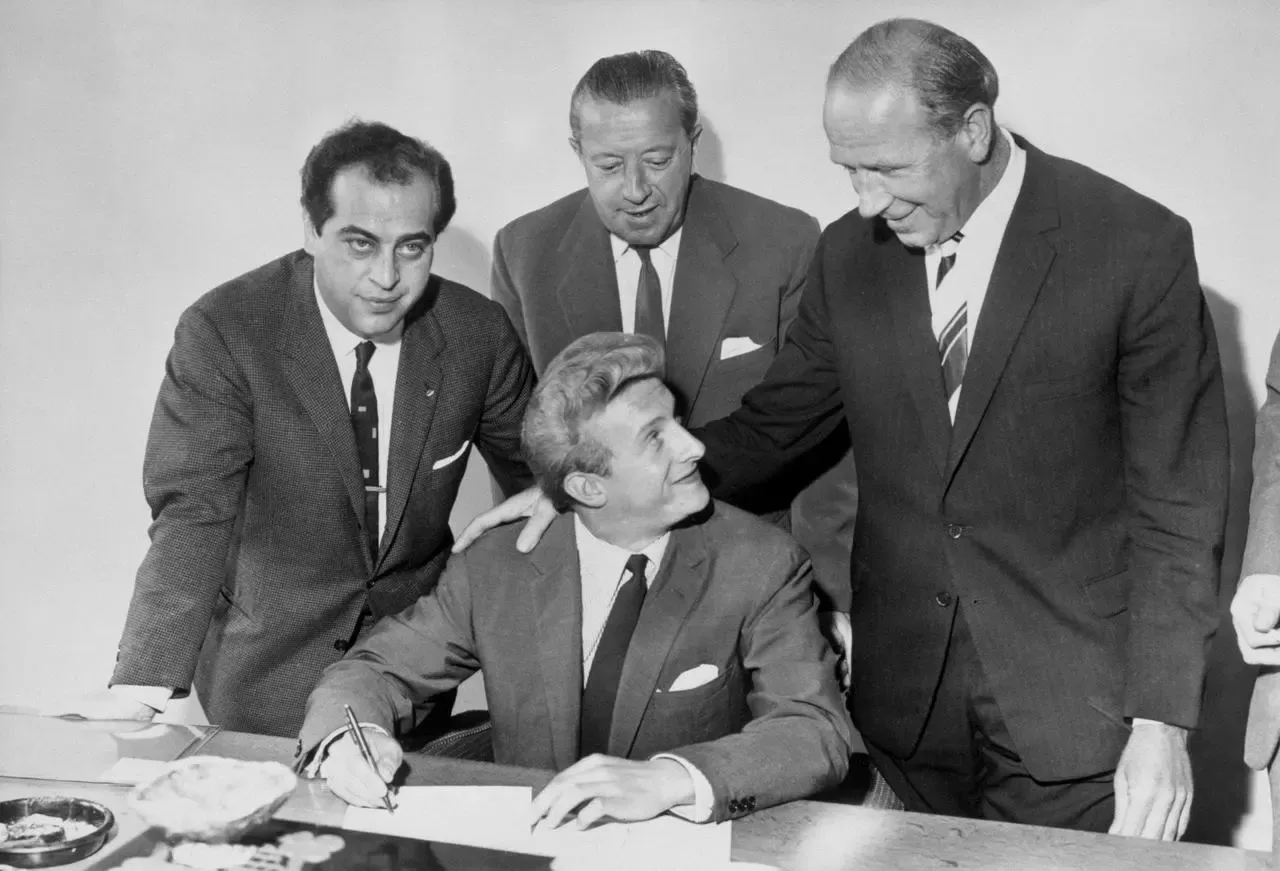 Denis Law (centre) smiles at Manchester United manager Matt Busby (right) as he puts pen to paper