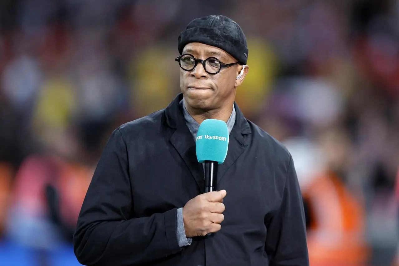 Ian Wright stands pitchside holding a microphone