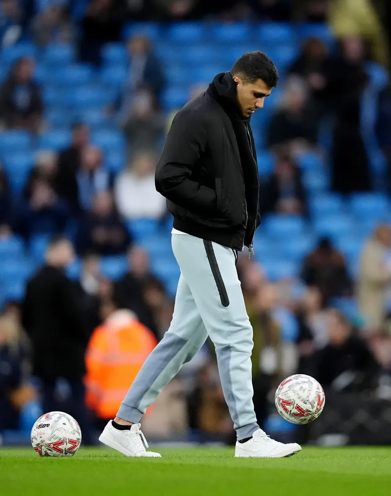 Manchester City's injured star Rodri, wearing a tracksuit, kicks a ball on the Etihad Stadium pitch