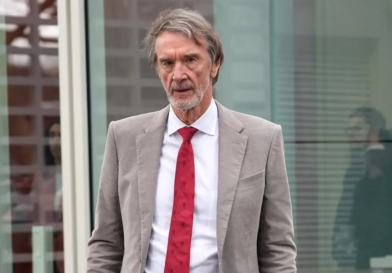 Manchester United co-owner Sir Jim Ratcliffe standing outside a building wearing a grey jacket and red tie