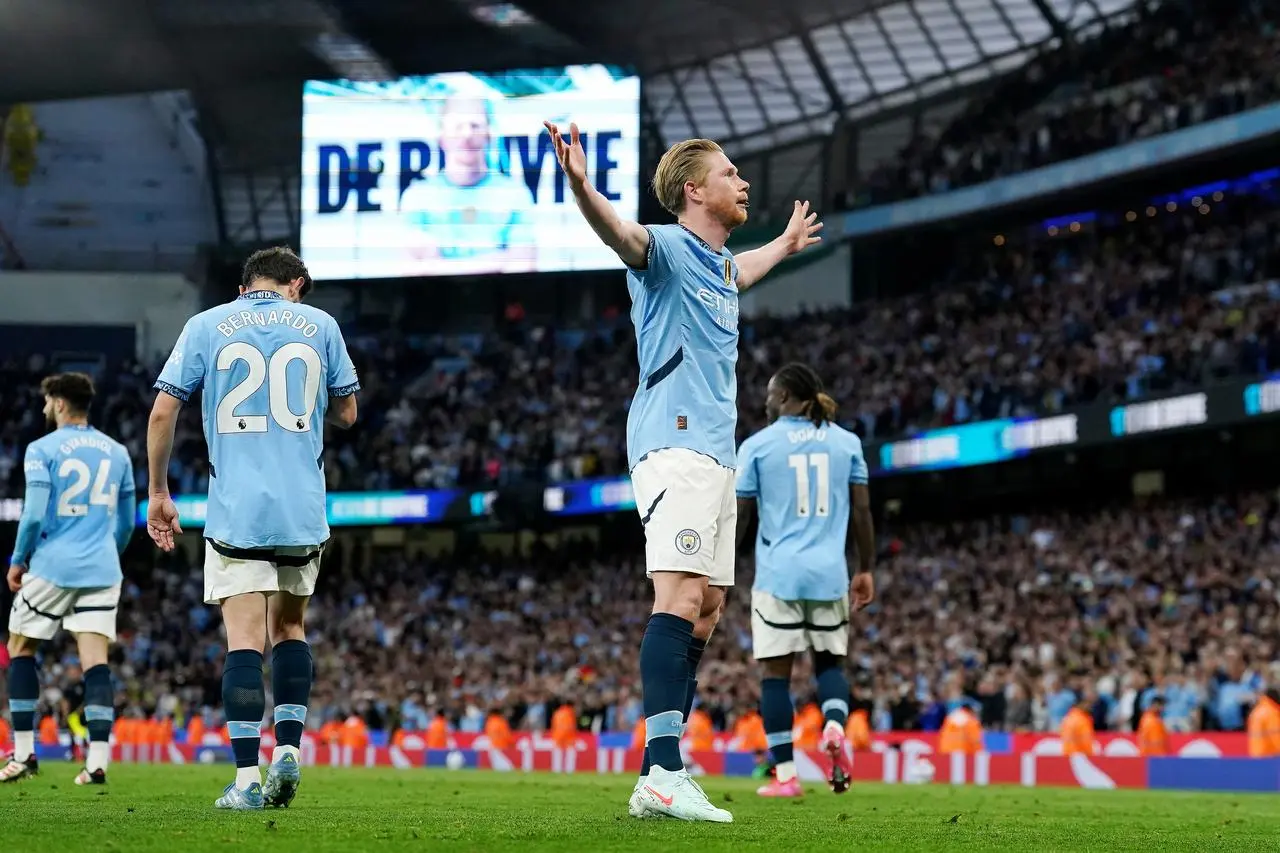 Kevin De Bruyne stands with his arms aloft in celebration